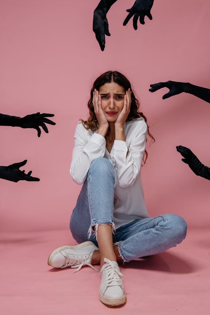 Tratamiento de Ansiedad y Depresión A woman looks anxious and stressed, sitting against a pink backdrop with hands reaching towards her.