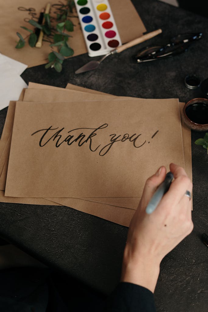 Gracias! Artist hand crafting a thank you card with calligraphy on brown paper.
